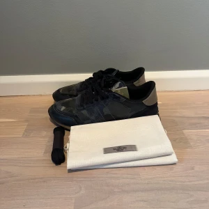Valentino Rockrunner sneakers camo blåa - Snygga Valentino Rockrunner sneakers med camouflagemönster. Skorna har svarta snören, rund tå och detaljer i mocka och skinn. Klassisk gummisula och ikoniska nitar på hälen. Kommer med dustbag och extra skosnören. Storlek 42 passar också 43. Skriv vid frågor!