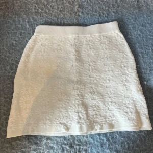 Vit blommig kortkjol från Zara - Supersöt vit kortkjol från Zara med upphöjt blommönster över hela tyget. Kjolen har en bred, ribbad midja som sitter skönt och ger en snygg passform. Perfekt för dig som gillar en fräsch och somrig look med lite extra detalj.