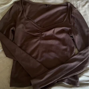 Svart långärmad topp - Snygg brun långärmad topp med ribbad struktur och lätt rynk vid bysten för en schysst detalj. Djupare ringning framtill som ger en modern vibe. Perfekt att styla med jeans eller kjol för en chill look.
