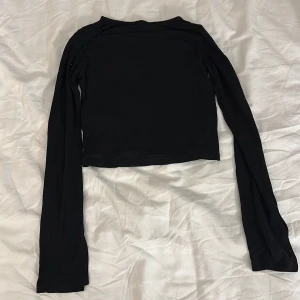 Svart långärmad topp Gina Tricot - En svart långärmad topp från Gina Tricot i enkel och stilren design. Modellen är croppad och har rund halsringning. Perfekt att matcha med jeans eller kjol för en clean look.