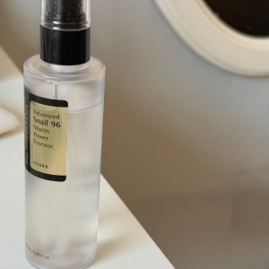 COSRX Snail 96 Mucin Essence - COSRX Advanced Snail 96 Mucin Power Essence i genomskinlig plastflaska med svart pump. Essencen är lätt och geléaktig, perfekt för att boosta fukt och ge glow till huden. Innehåller 96% snigelsekretfiltrat för extra återfuktning och lyster.