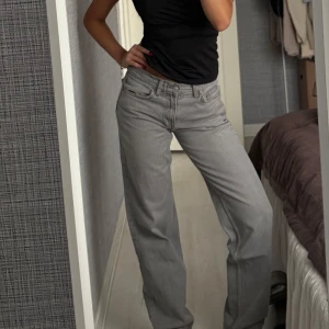 Grå raka jeansbyxor - Säljer ett par grå jeansbyxor med rak passform och låg midja. Byxorna har klassisk femficksdesign och stängs med dragkedja och knapp. Perfekta till en enkel topp eller hoodie.