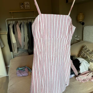 Röd- och vitrandig miniklänning från Pull&Bear - Säljer en  röd- och vitrandig klänning från Pull&Bear i storlek S. Klänningen har smala axelband, rak halsringning och smockad rygg för extra komfort.