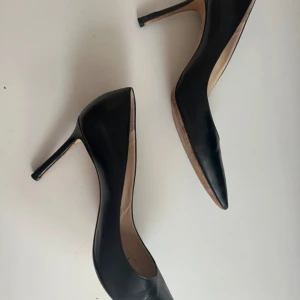 Svarta pumps från Jimmy Choo 38 - Säljer ett par klassiska svarta pumps från Jimmy Choo i skinn. Skorna har spetsig tå och hög klack, perfekt för dig som vill ha en tidlös och elegant look. Passar till många olika tillfällen och är riktigt snygga på foten. Klack 8,5 cm. Box ingår 