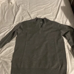 Grå halvzip tröja - Säljer en stilren grå tröja med halv dragkedja i halsen. Tröjan har långa ärmar och ribbade muddar vid ärmslut och nederkant. Perfekt för lager-på-lager och passar till många olika outfits. Den är väldigt mjuk och skön som du kan ha på sommaren och vintern.