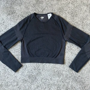 Svart croppad träningströja från 157 - Säljer en svart croppad långärmad träningströja från 157. Tröjan är tillverkad i ett stretchigt syntetmaterial och har en tight passform, perfekt för träning. Enkel och stilren design med rund halsringning.