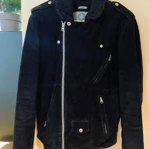 Svart fodrad mockajacka  - Säljer en svart fodrad mockajacka från Human Scales silvriga dragkedjor fina detaljer. Jackan har klassisk bikerstil med sned dragkedja, fickor med dragkedja och krage med pälsdetalj. Perfekt för kyliga dagar under både höst, vinter och vår. 