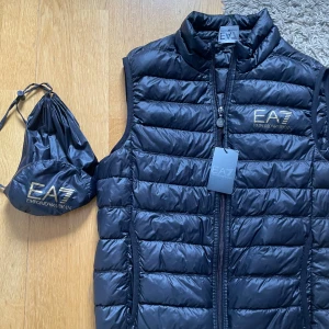 Emporio Armani EA7 Väst - Svart dunväst från Emporio Armani - Västen är helt ny, finns inga tecken på användning och har visa etiketter kvar - Den kommer även med original påse (se bilder) - Ord.pris 1400kr