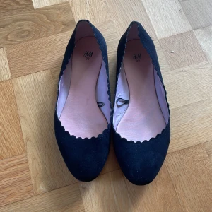 Svarta ballerinaskor med vågig kant från H&M - Säljer ett par svarta ballerinaskor från H&M i storlek 38. Skorna har en snygg vågig kant runt öppningen och rundt tå💕