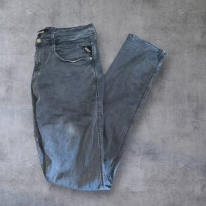 Svarta jeans från Replay - Säljer ett par svarta jeans från Replay med klassisk femficksdesign och diskret Replay-logga på fickan. Jeansen har raka ben och slim fitt passform, perfekta för en stilren look.