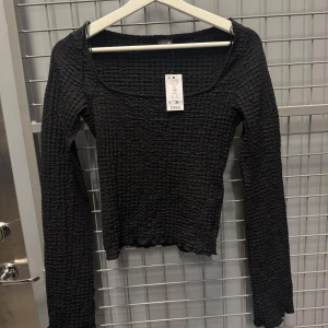 Svart ribbad topp med fyrkantig ringning - Svart långärmad topp med ribbad struktur och fyrkantig ringning. 