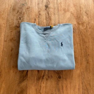 Polo Ralph Lauren – Sweatshirt i ljus isblå ton - Tidlös sweatshirt i en fräsch, sval färg med ton-i-ton-broderad logga. Ett mångsidigt basplagg med vintagekänsla.  Storlek: M (normal i storlek) Färg: Ljusblå med mörkblå logga Material: (komplettera gärna vid behov – t.ex. bomull/polyester) Skick: Mycket fint skick – inga synliga defekter Stil: Minimalistisk / Vintage / Avslappnad Passform: Klassisk rak modell med rund hals och ribbade muddar Nypris: ca 1 300 kr Pris: 290 kr  Frakt: Skickas snabbt & spårbart