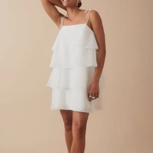 Vit volangklänning med smala axelband - Superfin vit klänning med flera lager volanger och smala axelband. Bara använd en gång! Klänningen har en luftig och lätt känsla, perfekt för varma dagar. Den är kort och har en lös passform som ger en avslappnad men ändå stilren look.