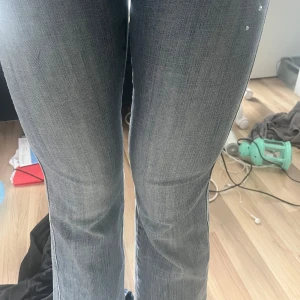 Grå bootcut jeans med fina detaljer  - Säljer ett par grå bootcut jeans med snygga nitar på ena sidan upptill. Jeansen har klassisk femficksdesign och normal passform. Perfekta för dig som vill ha en cool och avslappnad stil.
