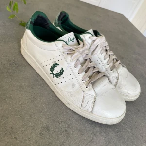 Fred Perry  - Fred Perry skor i färgen vit med gröna detaljer  ganska bra skick och perfekt för dig som vill ha stilren look i sommar. Finns vissa skavanker (se bild) nypris 1400