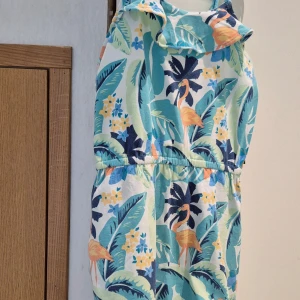 Färgglad sommarklänning med flamingomönster från Polarn O. Pyret - Säljer en söt och färgglad klänning från Polarn O. Pyret i storlek 134/140. Klänningen har smala axelband och ett tropiskt mönster med flamingos, blad och blommor i blått, grönt, gult och orange. Perfekt för varma dagar!