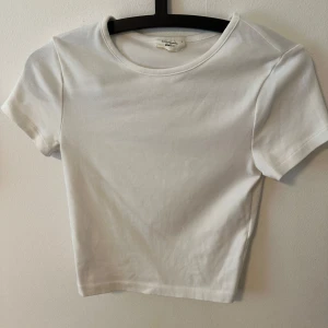 Vit croppad t-shirt - Säljer en enkel och stilren vit croppad t-shirt med rund halsringning och korta ärmar. Perfekt att matcha med jeans eller kjol för en avslappnad look.