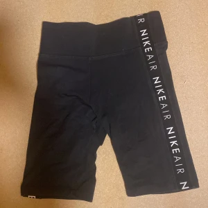 Svarta cykelshorts från Nike Air - Svarta cykelshorts från Nike Air med vit logga framtill och längs ena benet. Tight passform och elastisk midja. Perfekta för träning eller en sportig look. Tillverkade i mjukt och stretchigt syntetmaterial.
