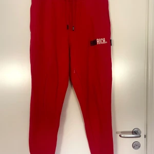 Röda mjukisbyxor från Hoodrich - Säljer ett par röda mjukisbyxor från Hoodrich med svart och vit logga på ena benet. Byxorna har dragsko i midjan och smal passform. Perfekta för chill eller träning.