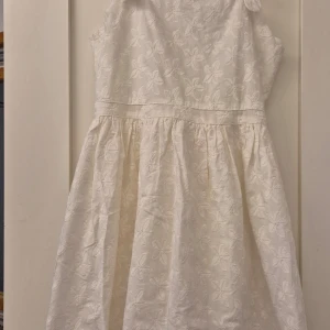 Ny Klänning polarn och pyret  - Söt vit klänning med broderade blommor och breda axelband. Klänningen har en lätt utställd kjol och dragkedja i ryggen. Perfekt för sommarens alla tillfällen!