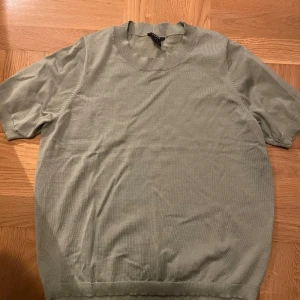 Ljusgrön stickad kortärmad tröja från Lindex - Säljer en ljusgrön stickad tröja från Lindex med korta ärmar och rund halsringning. Tröjan har ribbade muddar vid ärmslut, hals och nederkant. Perfekt för lager-på-lager eller sommarens svalare dagar.