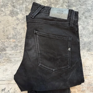 Svarta Replay jeansbyxor - Säljer ett par svarta jeans från Replay med klassisk femficksdesign och raka ben. Byxorna har en snygg svart tvätt, normal passform och läderpatch med Replay-logga bak i midjan. Midjemått W28 och längd L32.
