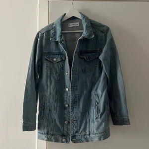 Ljusblå jeansjacka från Mango - Klassisk ljusblå jeansjacka från MNG med silverfärgade knappar framtill och på bröstfickorna. Jackan har lång ärm, två bröstfickor med lock och två sidofickor. Perfekt för lager-på-lager och enkel att styla.