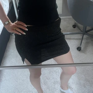 Svart glittrig minikjol - Säljer en svart minikjol med glittrigt tyg och liten slits på sidan.