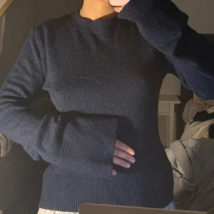 Mörkblå stickad tröja - Mysig mörkblå stickad tröja med rund halsringning och långa ärmar. Tröjan har en enkel och stilren design med ribbade muddar vid ärmslut och nederkant. Perfekt för kyligare dagar.