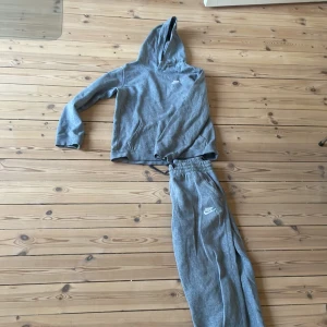 Grå mjukisbyxor och hoodie från NIKE - Säljer ett par grå mjukisbyxor och en likadan färgad hoodie från Nike. De är i mjukt bomullsmaterial och har en avslappnad passform, perfekta för chill eller träning. Både hoodien och byxorna är i storlek 158-170cm. Har använt typ 2-3 gånger. Skriv bara om funderingar! 
