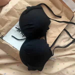 Svart bikiniöverdel med knyt - Säljer en svart bikiniöverdel med vadderade kupor och knyt i nacken och ryggen. Enkel och stilren design som passar perfekt till sommaren. Bikinin har en klassisk form och är tillverkad i ett mjukt material. Pris kan självklart diskuteras. Våga ställa frågor vid funderingar. 