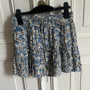 Blommig volangkjol i blått och vitt - Supersöt kortkjol med blått och vitt blommönster. Kjolen har volanger och resår i midjan. Perfekt till sommaren! Den är bra skick.💕