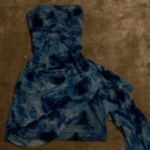 Blå axelbandslös omlottklänning - Säljer en blå axelbandslös klänning med omlott-detalj och draperad effekt. Klänningen har ett unikt batikmönster i olika blå nyanser och en lång släp på sidan. Den är köpt i Istanbul för runt 600 kronor och är även helt oanvänd🤍