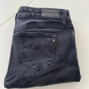 Svarta jeansbyxor från Replay - Säljer ett par svarta jeansbyxor från Replay med klassisk femficksdesign och raka ben. Byxorna har en diskret logga på bakfickan och Replay-märke vid fickan fram. Perfekta för dig som gillar stilrena och tidlösa jeans. Jeansen är i väldigt bra skick det är bara bilderna som är lite halvdana!