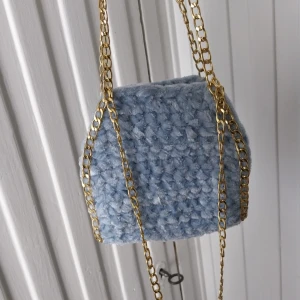 Ljusblå virkad handväska med guldkedja - Säljer en ljusblå virkad väska med grovt virkat mönster och snygg guldfärgad kedja. Perfekt för att lyfta din outfit med en unik accessoar. Väskan är mjuk och har en trendig look.