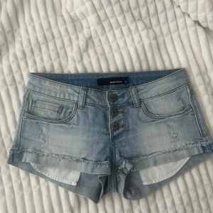 Ljusblå lågmidja jeansshorts - Säljer ett par lågmidja ljusblå jeansshorts med slitningar. Storlek 34/XS.