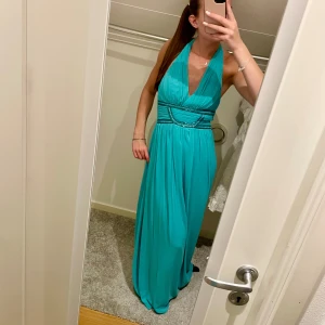 Turkos långklänning med halterneck - Säljer en turkos långklänning med halterneck och v-ringning. Klänningen har markerad midja med pärldetaljer och öppen rygg. Perfekt för bal eller fest! Flödande material som ger en elegant look.💙🦋aldrig använd! Pris kan diskuteras 💙