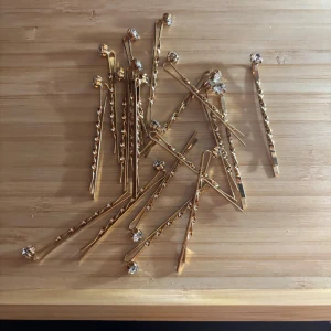 Guldiga hårnålar med glittriga stenar - Säljer ett gäng snygga guldiga hårnålar med glittriga stenar på toppen. Perfekta för att piffa till frisyren och ge lite extra bling till håret. Passar både till fest och när du vill känna dig lite extra glam.