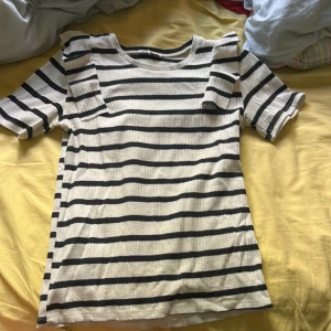 Randig ribbad topp med volangdetaljer från Zara - Säljer en vit ribbad topp med svarta horisontella ränder från Zara. Toppen har korta ärmar och volangdetaljer på axlarna som ger en trendig look 💗