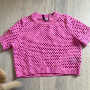 Rosa meshstickad topp från H&M - Säljer en rosa, kortärmad meshstickad topp från H&M. Tröjan har ett genombrutet mönster och ribbade kanter vid hals, ärmslut och nederkant. Perfekt för lager på lager och en färgklick i garderoben! Passar S men även mindre M