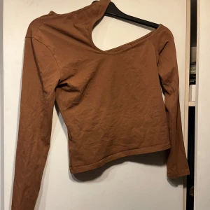 Brun oneshoulder topp från NA-KD - Säljer en brun långärmad topp från NA-KD med unik oneshoulder-design. Toppen är croppad och har en snygg asymmetrisk halsringning som ger en cool look. Perfekt att styla med jeans eller kjol för en trendig outfit. Priset är diskuterbart 
