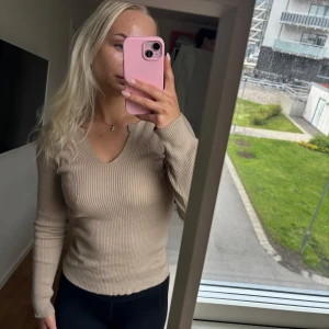 Beige ribbad långärmad tröja  - Säljer en beige ribbad tröja med v-ringad hals. Tröjan är figurnära och har långa ärmar. Perfekt att matcha med jeans eller kjol för en enkel och stilren look.