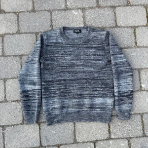 Gråmelerad stickad tröja från A.P.C. - Säljer en snygg gråmelerad stickad tröja från A.P.C. Tröjan har rund halsringning och långa ärmar. Perfekt för kyligare dagar och passar till det mesta. Klassisk och stilren design med ribbade muddar vid ärmslut och nederkant.