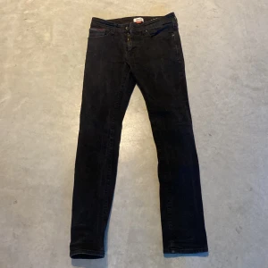 Svarta slim jeans från Hilfiger Denim - Säljer ett par svarta slim fit jeans från Hilfiger Denim. Klassisk femficksmodell med dragkedjegylf och diskret Hilfiger-detalj på bakfickan. Perfekta för dig som gillar en smalare passform och stilren look.