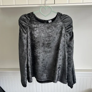 Grå tröja med puffärmar - Säljer en snygg grå tröja  med långa puffärmar och rund halsringning. Blusen har en glansig finish och är perfekt för dig som vill sticka ut lite extra. Stängs med knapp i nacken. Pris går att diskutera 