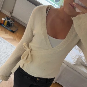 Vit omlottkofta med knytband - Mysig vit omlottkofta med knytband i midjan och långa ärmar. Tröjan har en djup v-ringning och är stickad i ett mjukt material ifrån Gina!💕