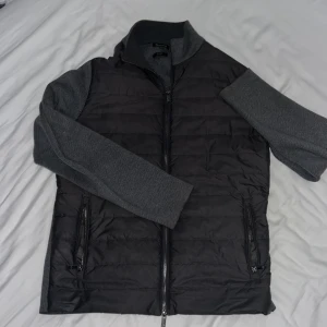 Grå hybridjacka från Massimo Dutti - Snygg grå hybridjacka från Massimo Dutti med quiltad framsida och stickade ärmar samt rygg. Jackan har dragkedja framtill och två fickor med dragkedja. Perfekt för lager-på-lager under kyliga dagar.