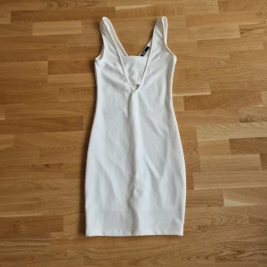 Vit tight kortklänning med v-ringning - Säljer en vit tight kortklänning från Bik Bok med djup v-ringning och breda axelband. Klänningen har en minimalistisk design och är tillverkad i ett stretchigt material som sitter snyggt på kroppen. Perfekt för dig som gillar stilrena och enkla plagg.