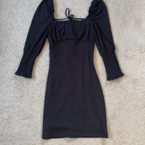 Svart miniklänning med knytning - Snygg svart klänning från Bikbok med öppen rygg, knytning där bak och fyrkantig urringning. I storlek XS. Endast använd en gång, som ny. Kommer tyvärr inte till användning ❤️