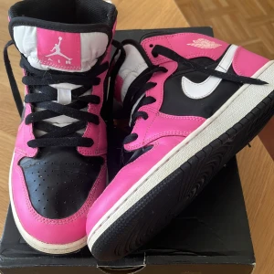 Nike Air Jordan 1 Mid GS svart/rosa/vit - SÄljer mina Jordan 1 i rosa vit och svart då dem är för stora för mig, använt några fåtal gånger och stått i förrådet, observera att snoddarna är ”avskurna” då de var för stora. Acceptabelt skick, därav priset, små creases. 